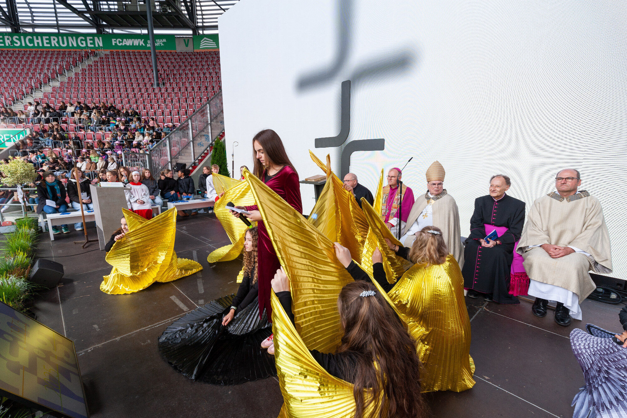 Sprecherin im roten Kleid vor knienden Flügel-Darstellerinnen, WWK Arena Augsburg / Schulwerk