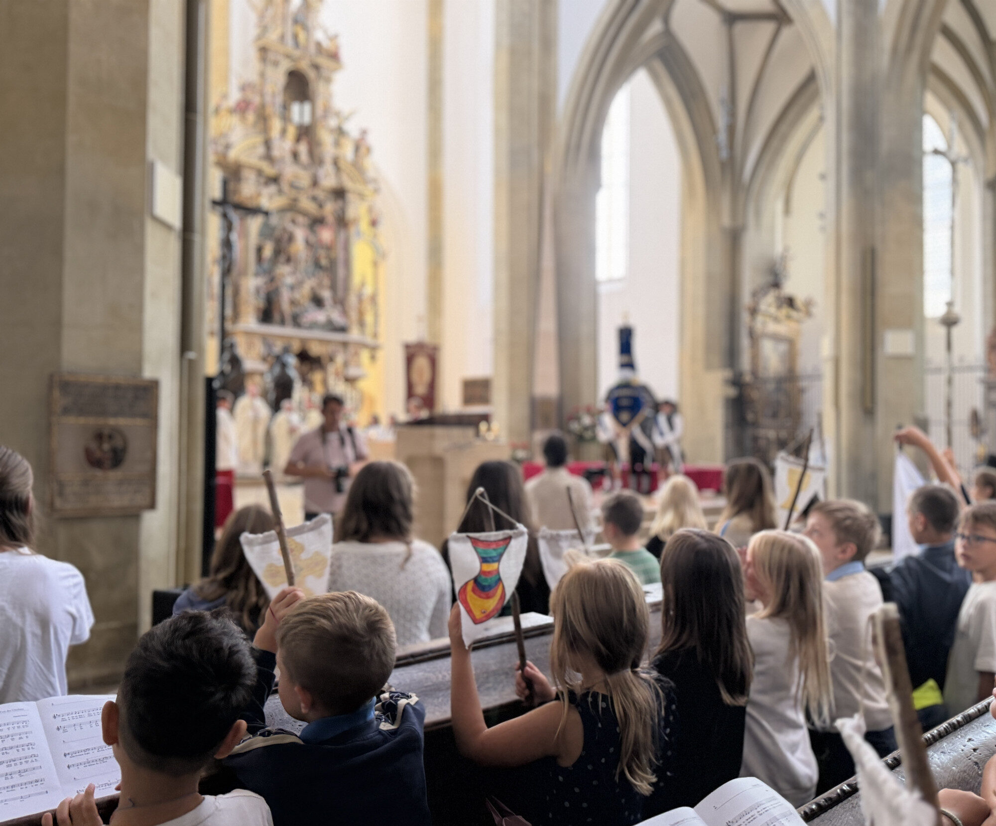 Schülerinnen und Schüler mit Fähnchen und Liedblättern beim Pontifikalamt der Ulrichswoche
