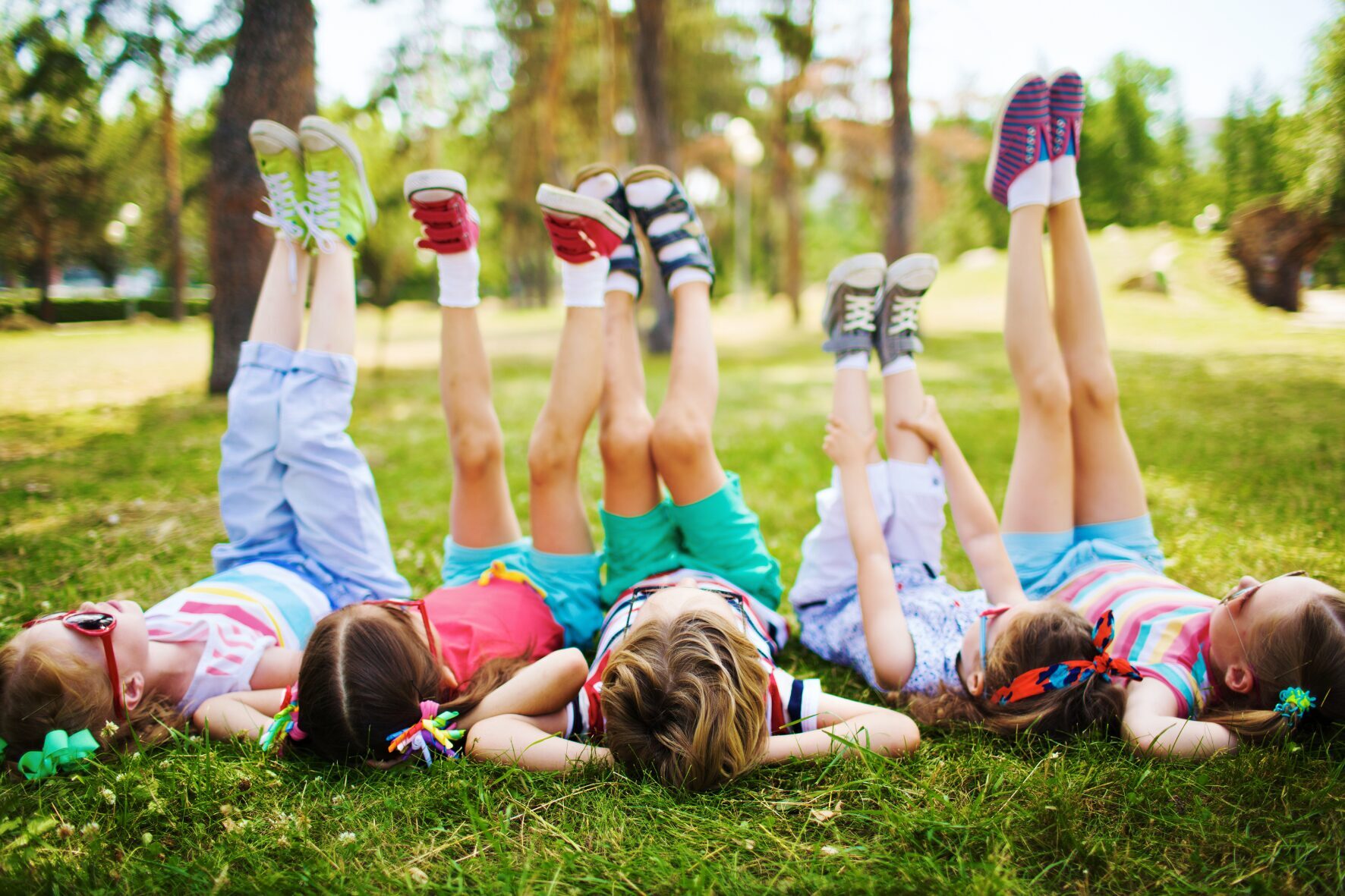 Kinder liegen im Sommergras mit hochgestreckten Beinen, Schulwerk der Diözese Augsburg