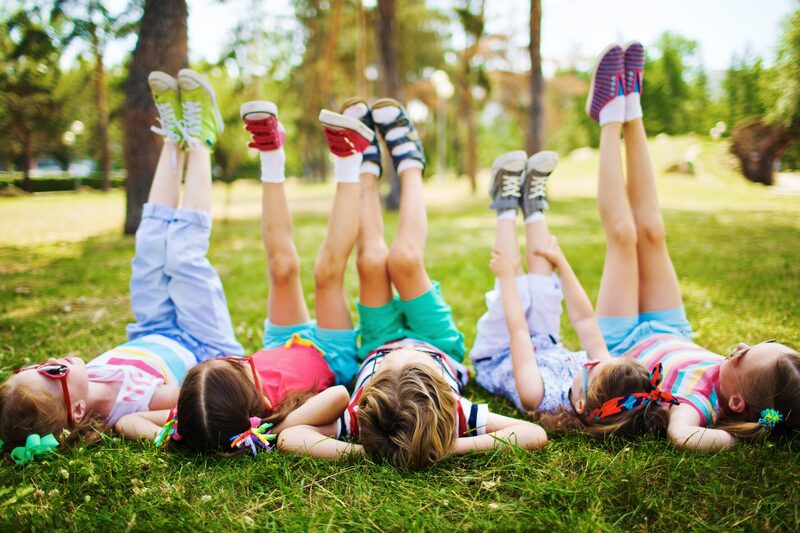 Kinder liegen im Sommergras mit hochgestreckten Beinen, Schulwerk der Diözese Augsburg